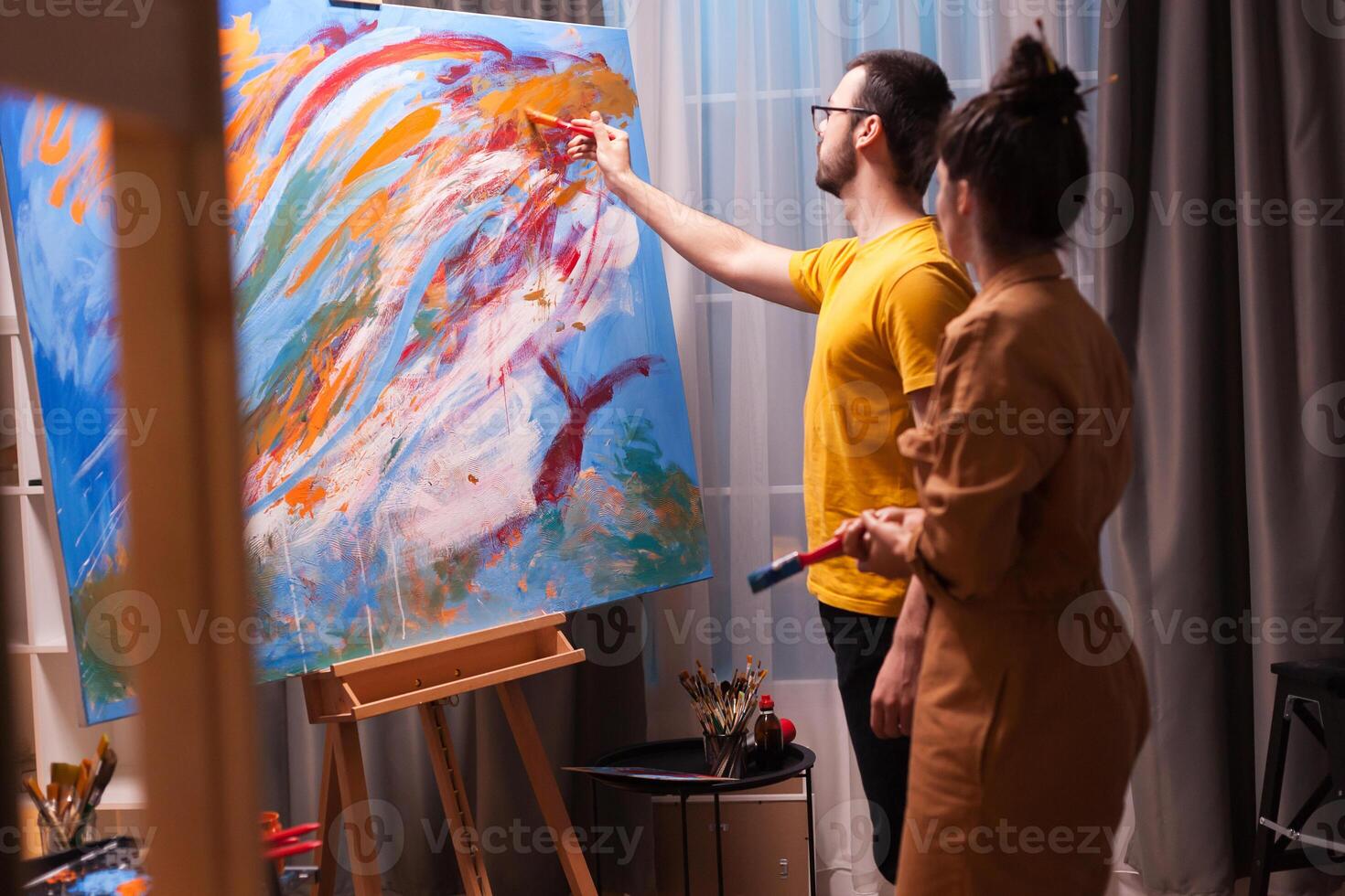Couple of artists talking and painting in their art workshop. Modern artwork paint on canvas, creative, contemporary and successful fine art artist drawing masterpiece photo