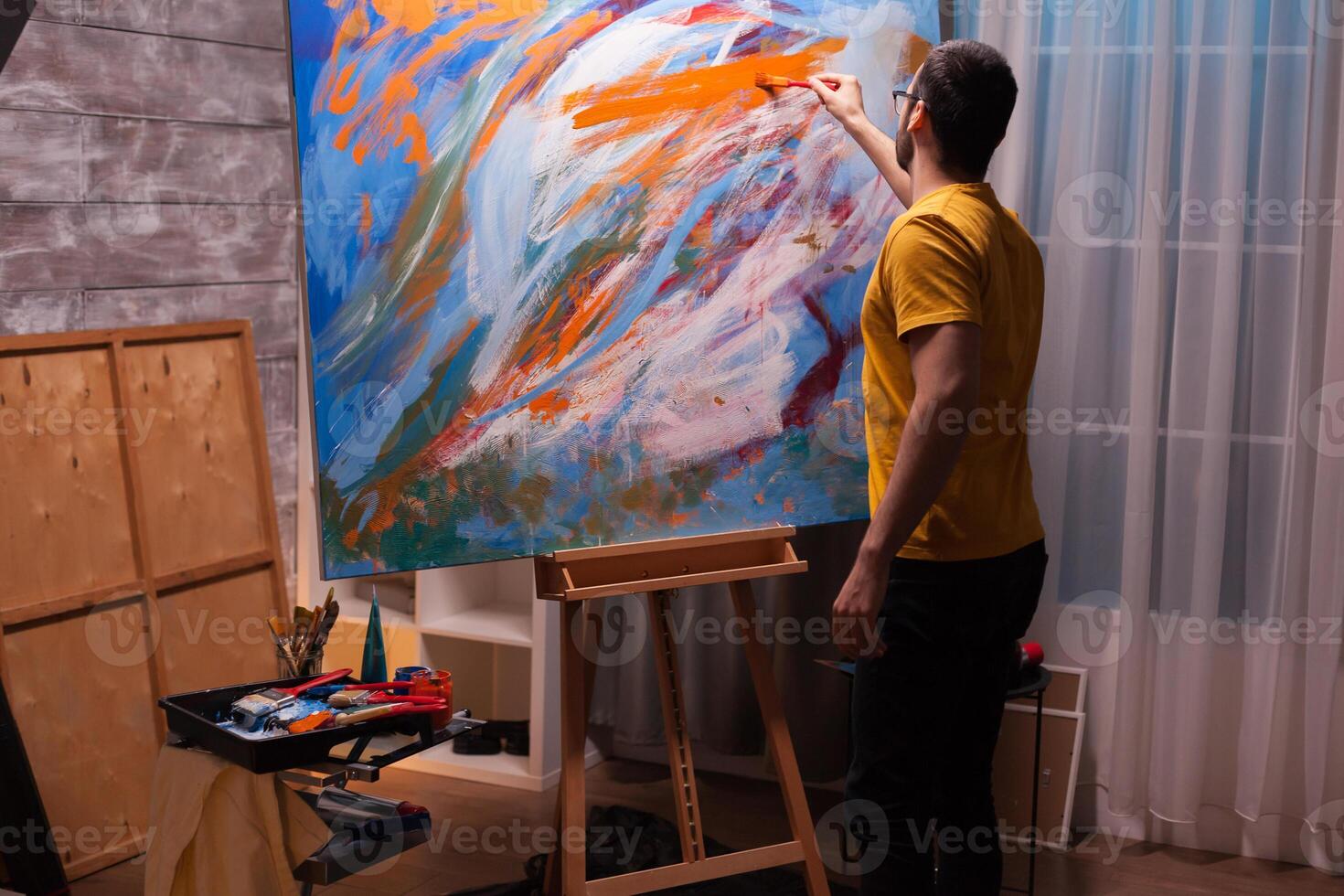 Young man with painting skill working on large canvas in art studio. Modern artwork paint on canvas, creative, contemporary and successful fine art artist drawing masterpiece photo