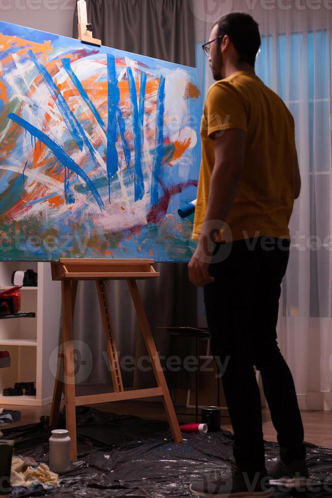 Abstract painter holding roller and looking at his masterpiece painting. Modern artwork paint on canvas, creative, contemporary and successful fine art artist drawing masterpiece photo