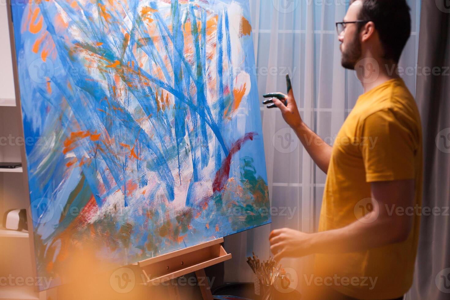 Young artist standing in front of painting in art workshop. Painting a masterpiece. Modern artwork paint on canvas, creative, contemporary and successful fine art artist drawing masterpiece photo