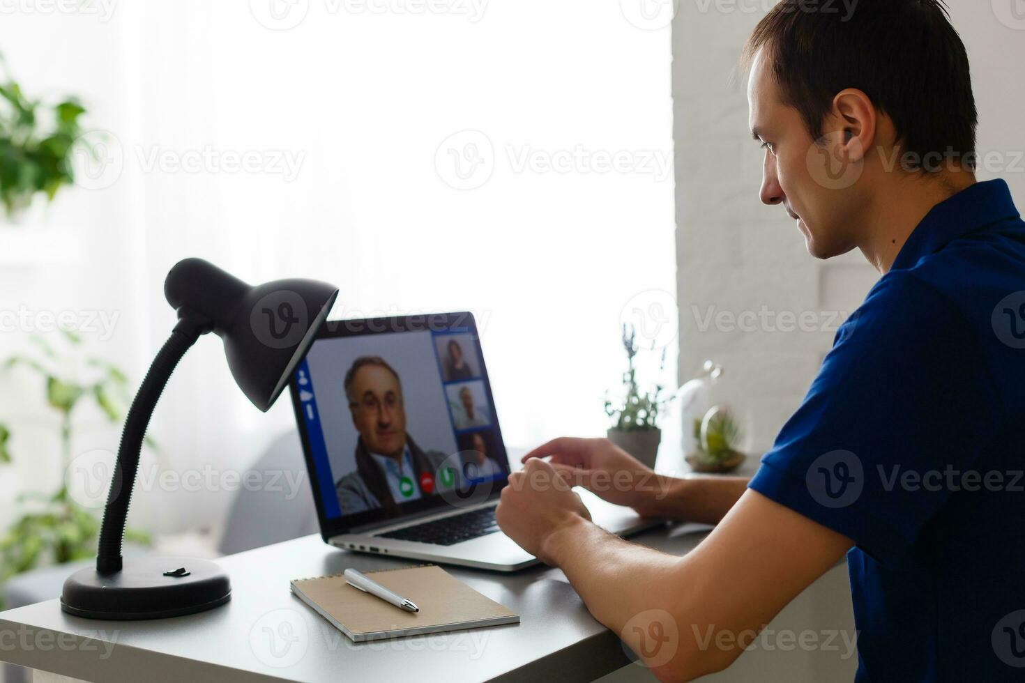 contento joven hombre en camiseta sentado a hogar, trabajando en ordenador portátil computadora, sonriente. foto