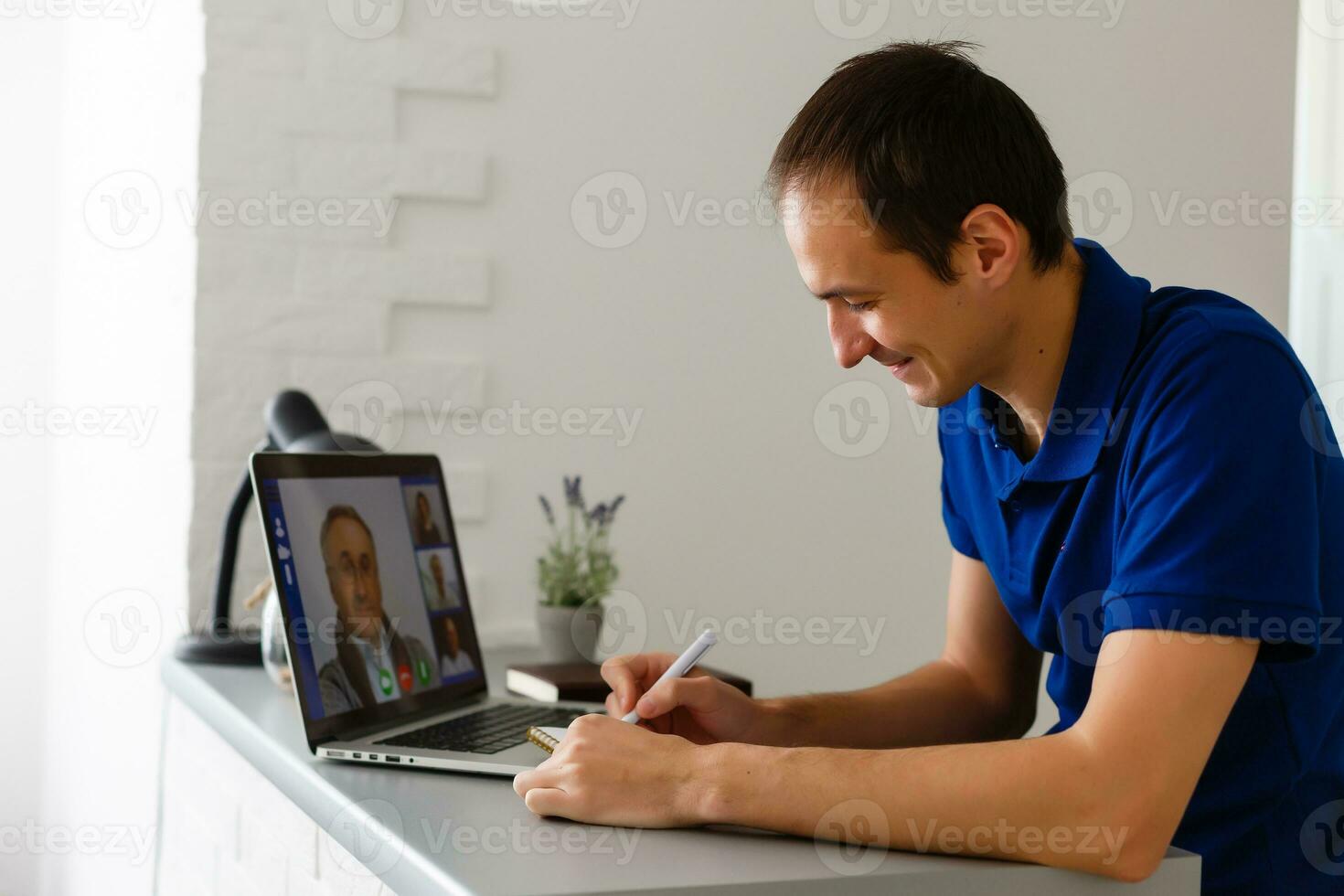Happy young man in t-shirt sitting at home, working on laptop computer, smiling. photo