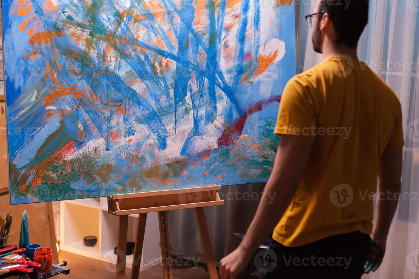 Young artist looking at his masterpiece in art workshop. Modern artwork paint on canvas, creative, contemporary and successful fine art artist drawing masterpiece photo