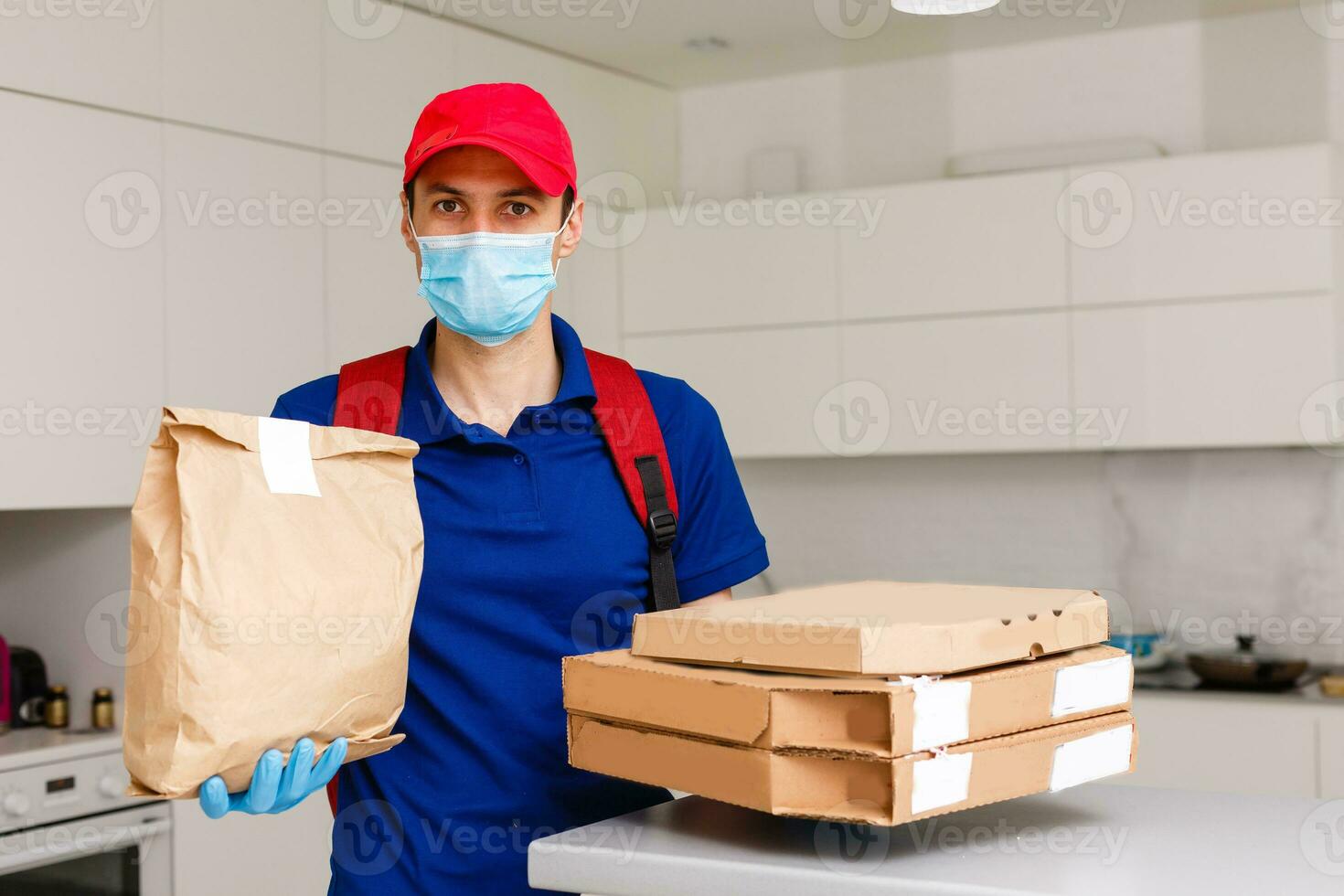 entrega hombre empleado en rojo gorra camiseta uniforme máscara guantes dar comida orden Pizza cajas aislado en amarillo antecedentes estudio. Servicio cuarentena pandemia coronavirus virus gripe 2019-ncov concepto foto