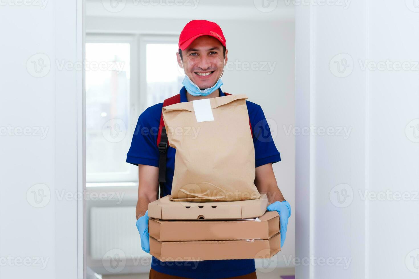 entrega hombre empleado en rojo gorra camiseta uniforme máscara guantes dar comida orden Pizza cajas aislado en amarillo antecedentes estudio. Servicio cuarentena pandemia coronavirus virus gripe 2019-ncov concepto foto