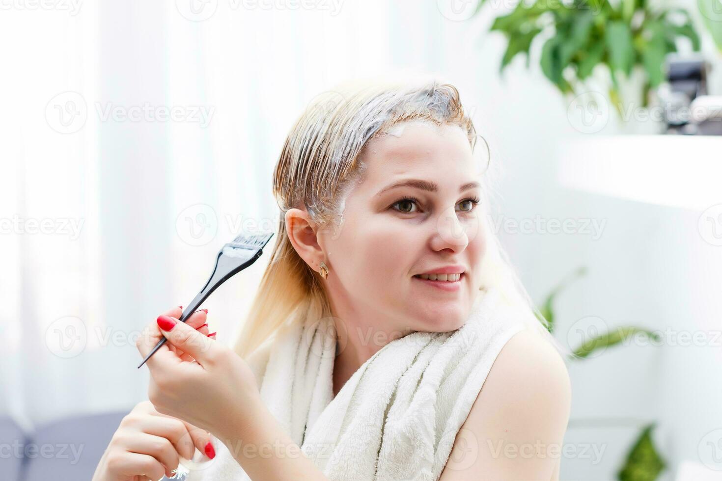 A middle-aged woman dyes her hair at home, indoors photo