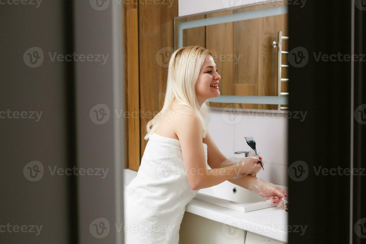 A middle-aged woman dyes her hair at home, indoors photo