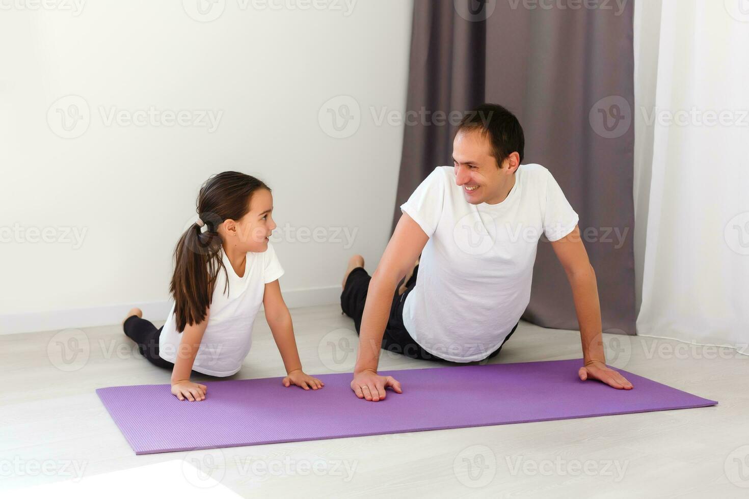 Handsome young father and his cute little daughter are doing reverce plank with leg raise on the floor at home. Family fitness workout. photo
