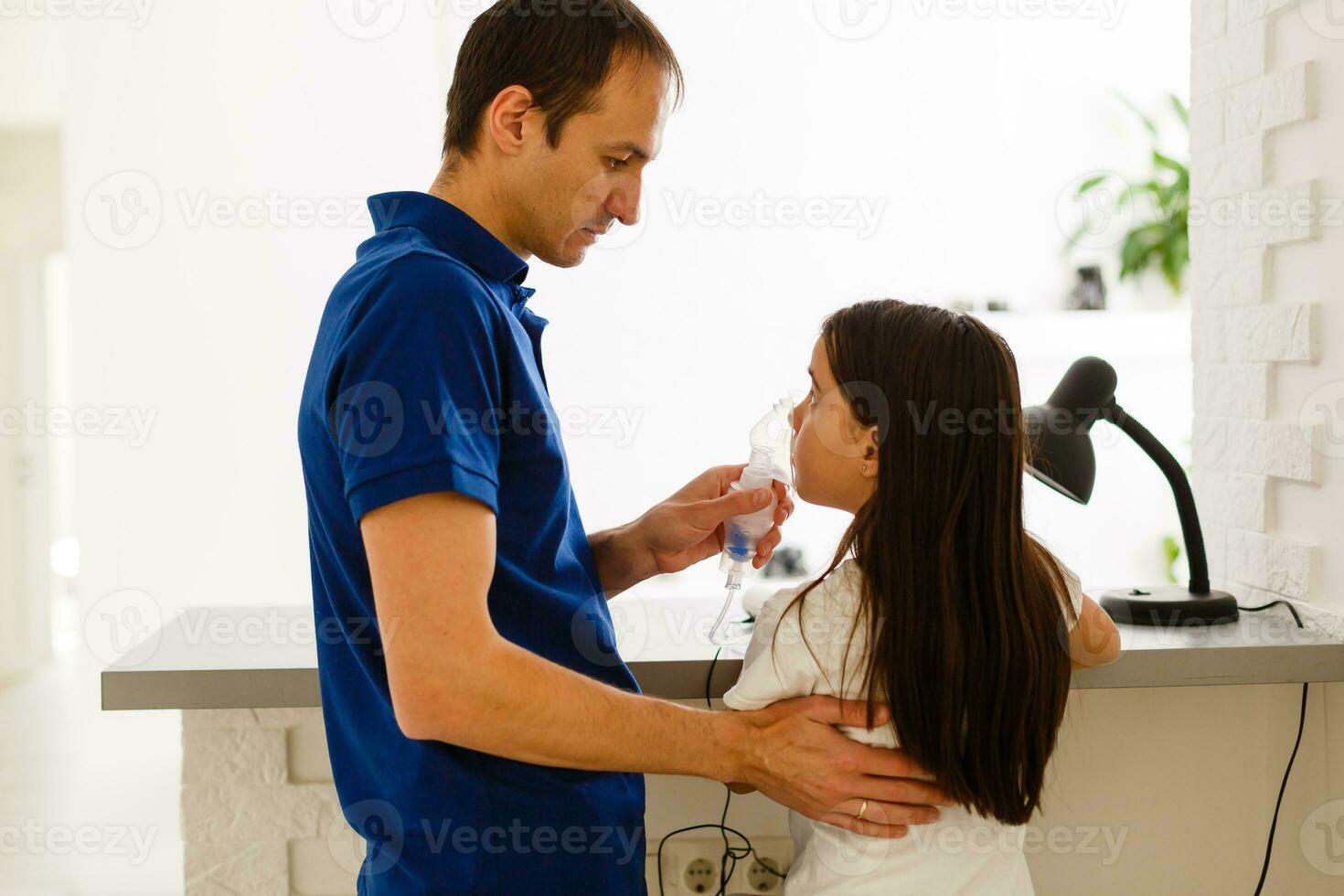 father and daughter do inhalations. caring dad helps her daughter breathe through the mask. treatment of respiratory tract. photo