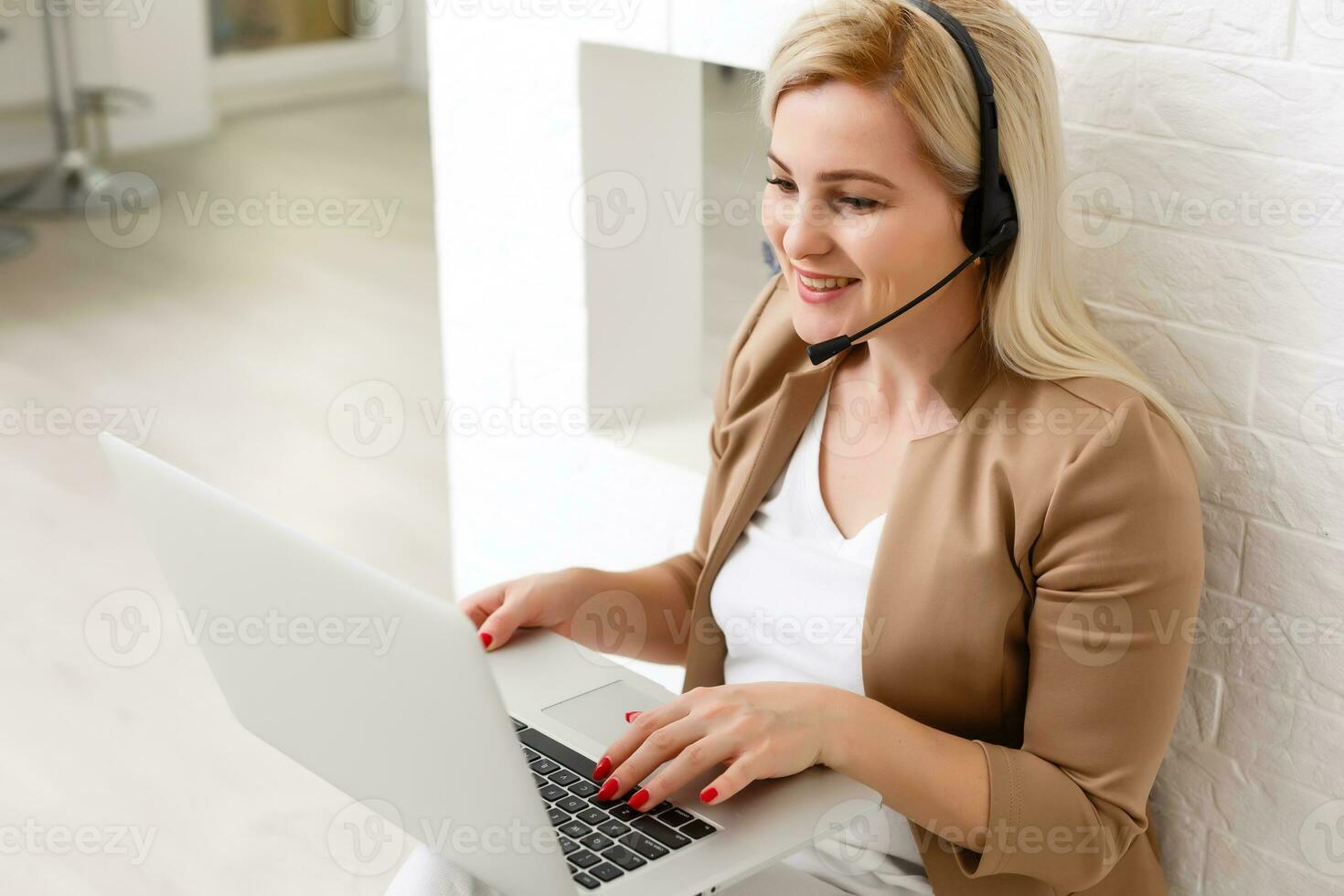 Focused attentive woman in headphones sits with laptop, looks at screen, makes notes, learns foreign language in internet, online study course, self-education on web, consults client by video photo