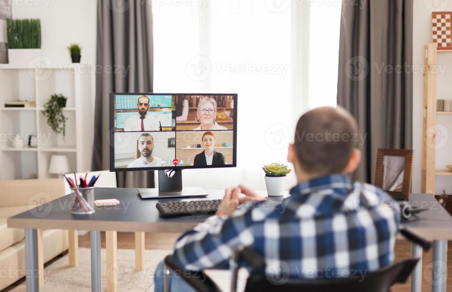 Disabled man in wheelchair during a video conference with work colleagues. Young immobilized freelancer doing his business online, using high technology, sitting in his apartment, working remotely in special conditions. photo