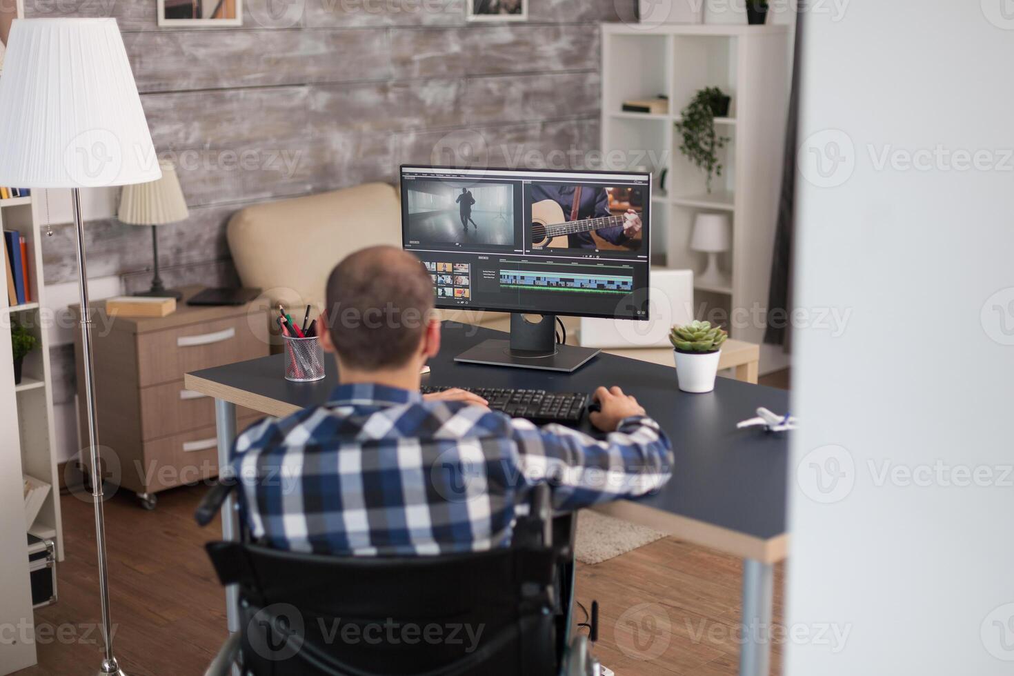 Video editor working from home sitting in wheelchair infront the computer. Invalid videographer doing his business online, using high technology, sitting in his apartment, working remotely in special conditions. photo