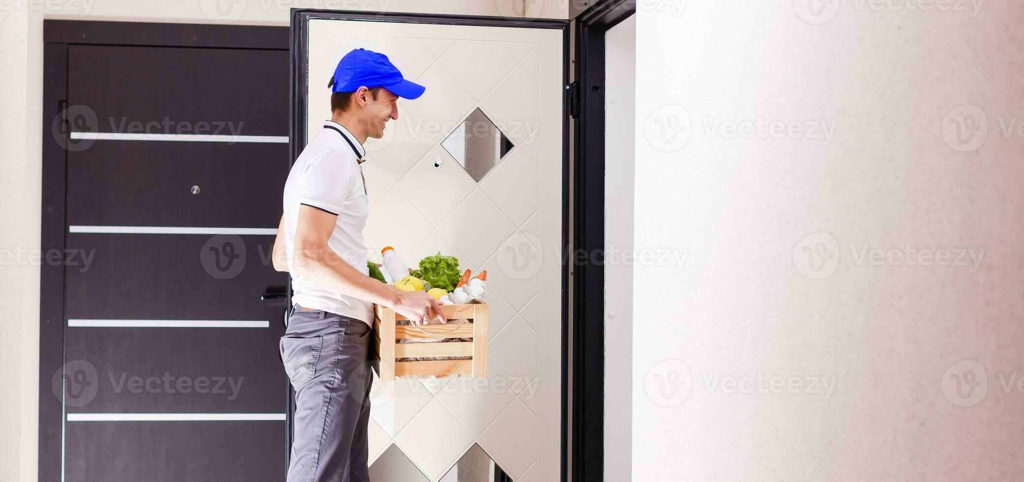 Fast and reliable service. Cheerful young delivery man giving a box to young woman while standing at the entrance of her apartment photo