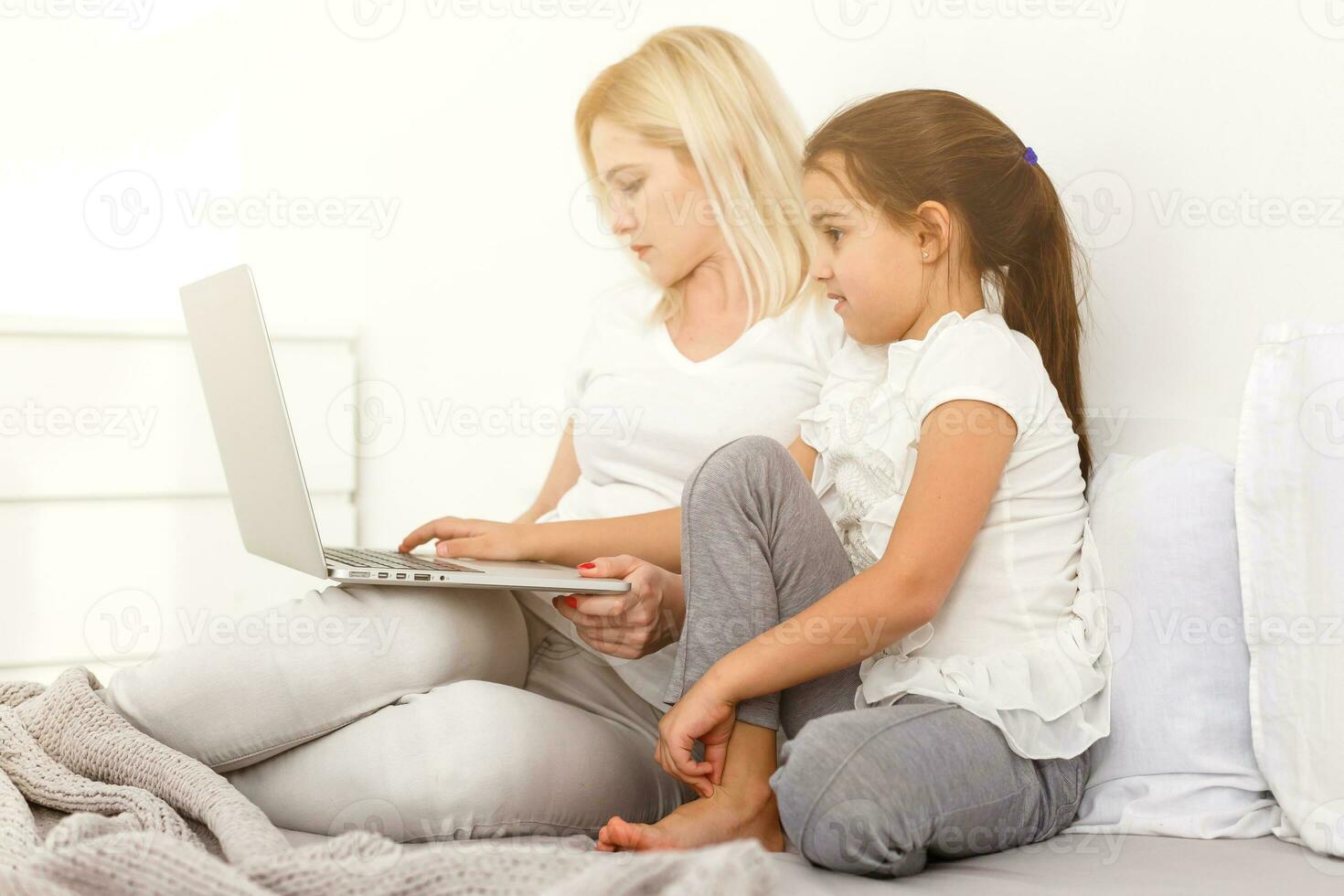 little girl and mother with laptop on the bed photo