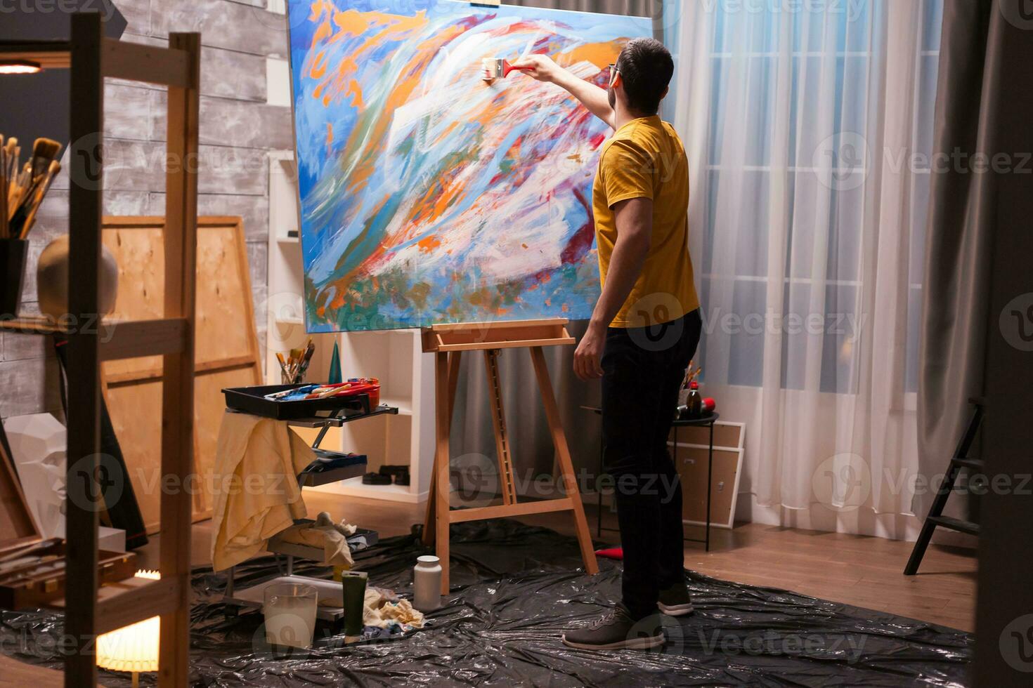 Talented young man painting on large canvas in studio. Modern artwork paint on canvas, creative, contemporary and successful fine art artist drawing masterpiece photo
