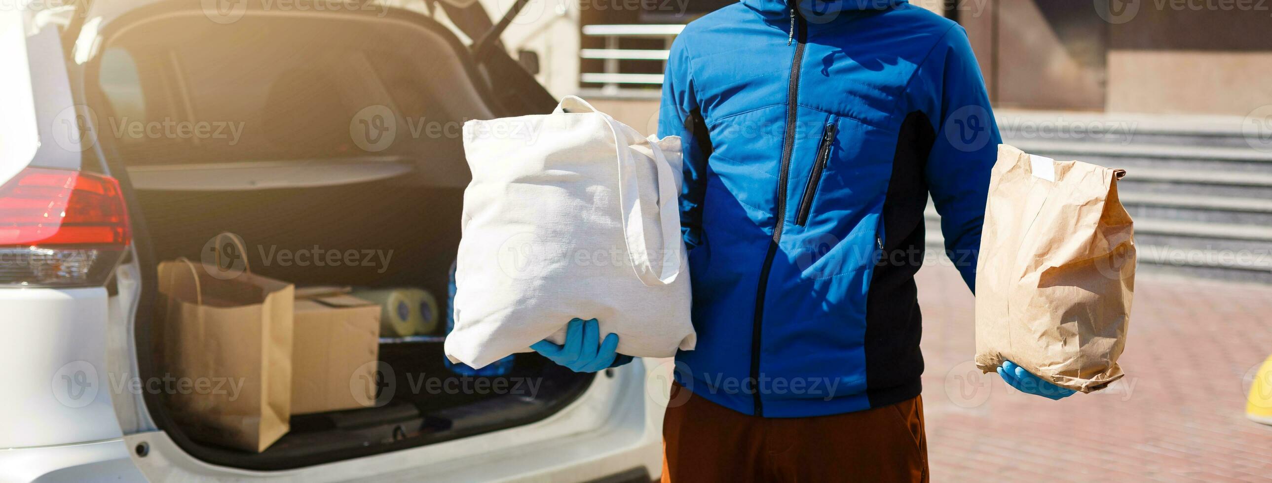 Delivery man holding paper bag with food near the car, food delivery man in protective mask photo