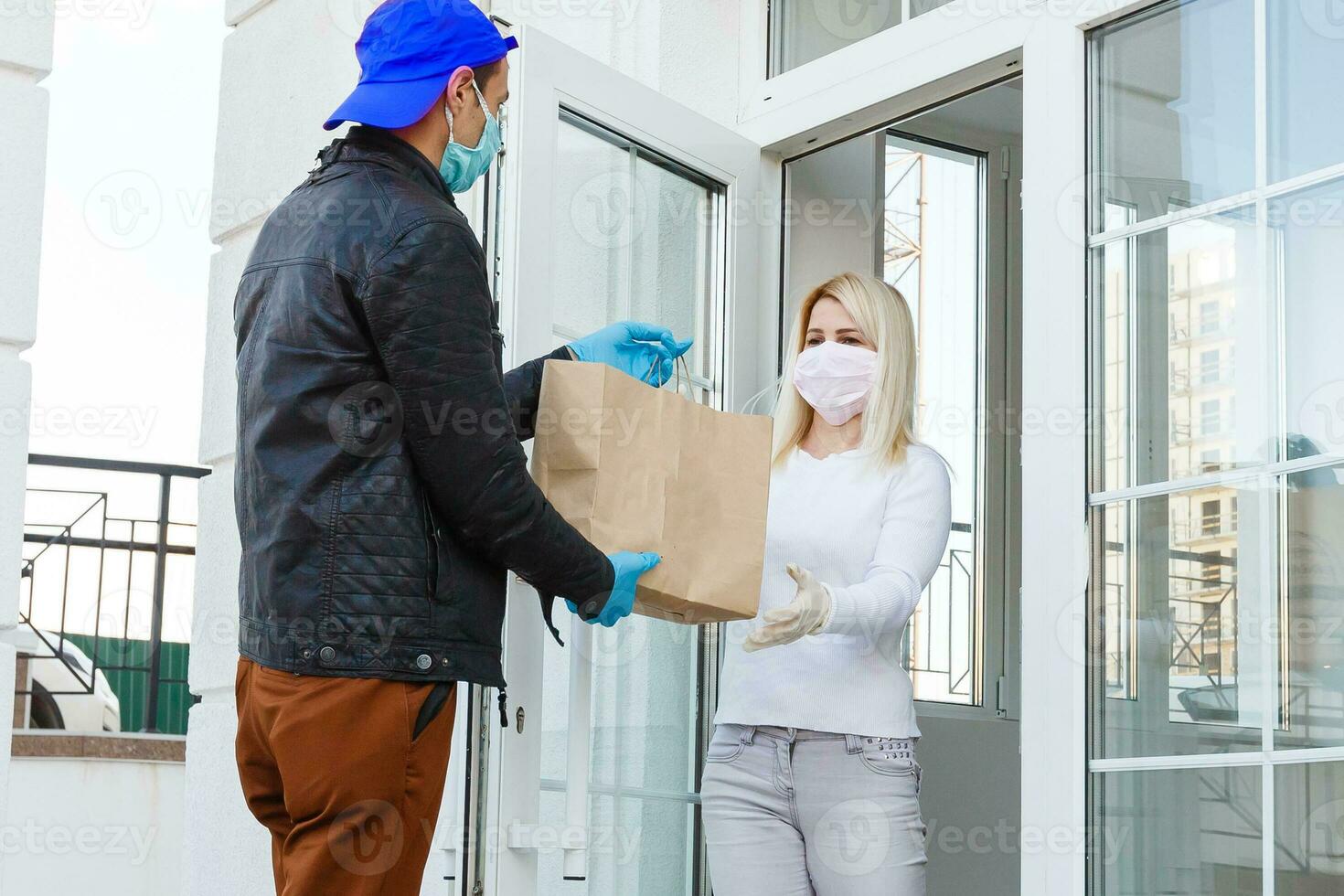 Courier, delivery man in protective mask and medical gloves delivers takeaway food. Delivery service under quarantine, disease outbreak, coronavirus covid-19 pandemic conditions. Stay home photo
