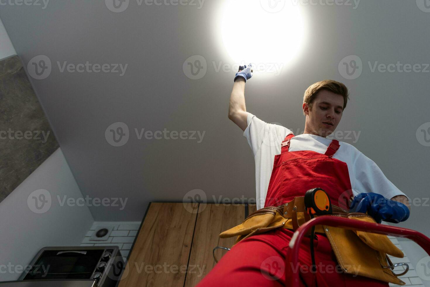 Worker installing lamp on stretch ceiling indoors. photo