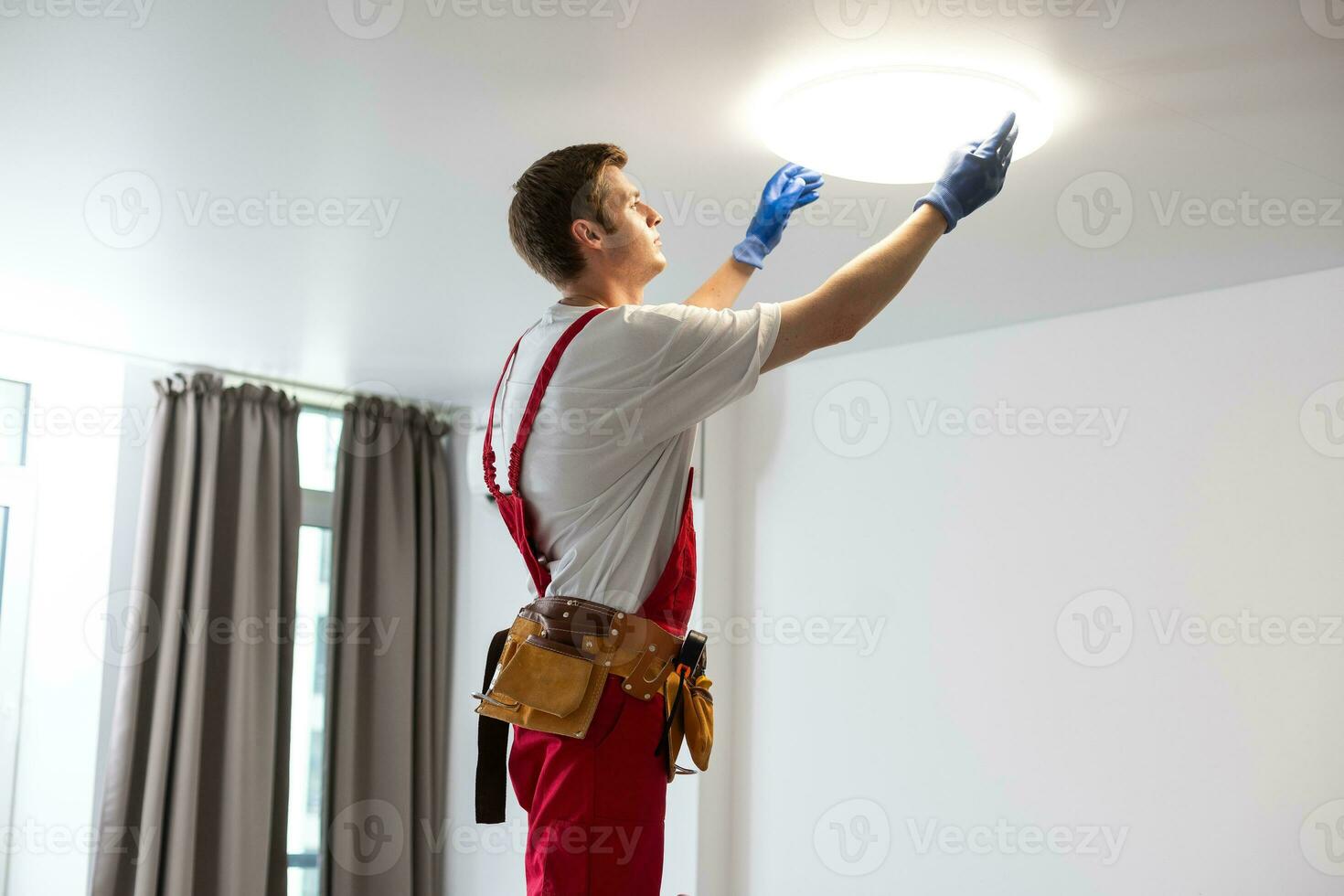 joven hombre instalando techo lámpara en escalera de tijera en cocina foto