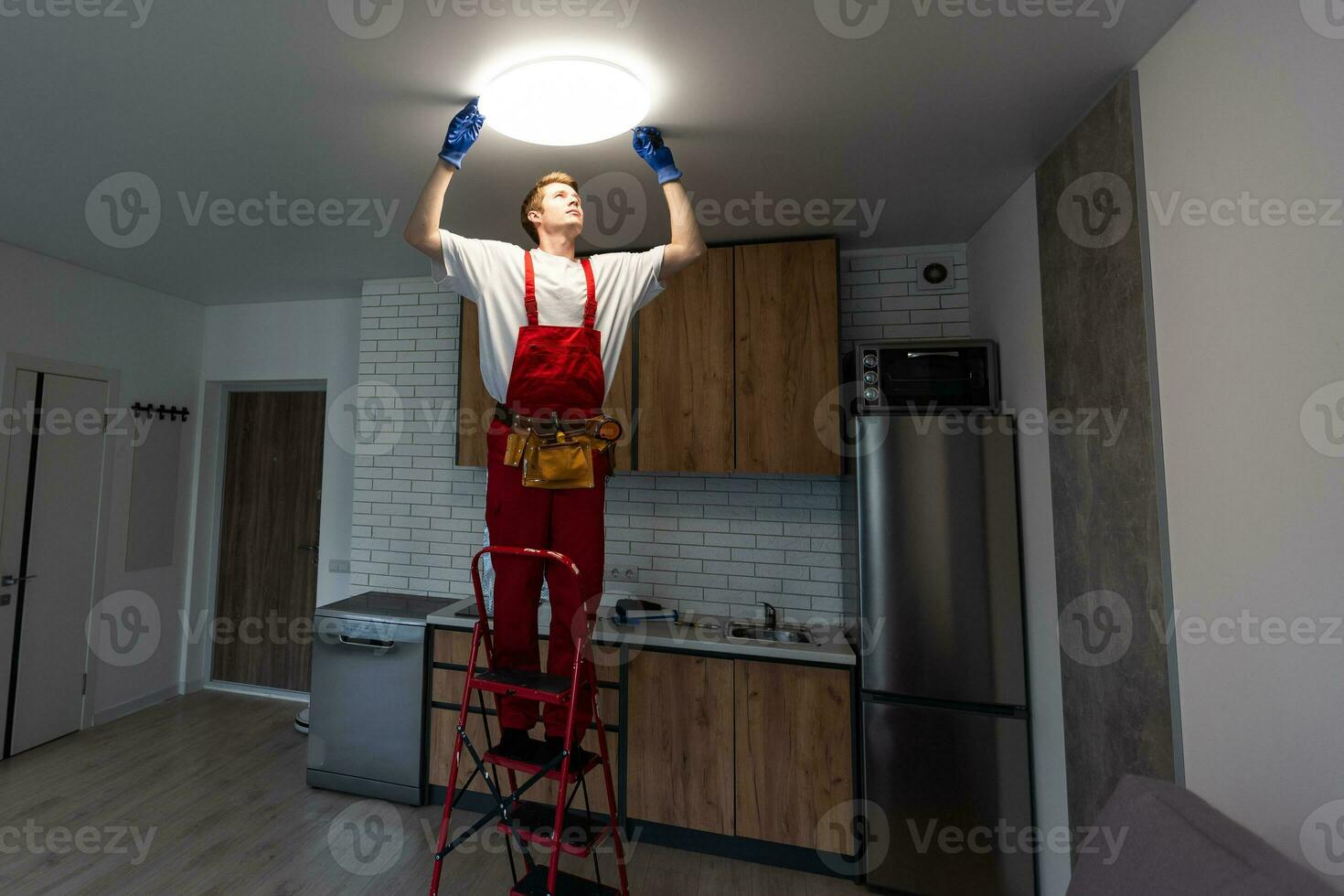 Electrician in uniform installing ceiling lamp indoors. Space for text photo