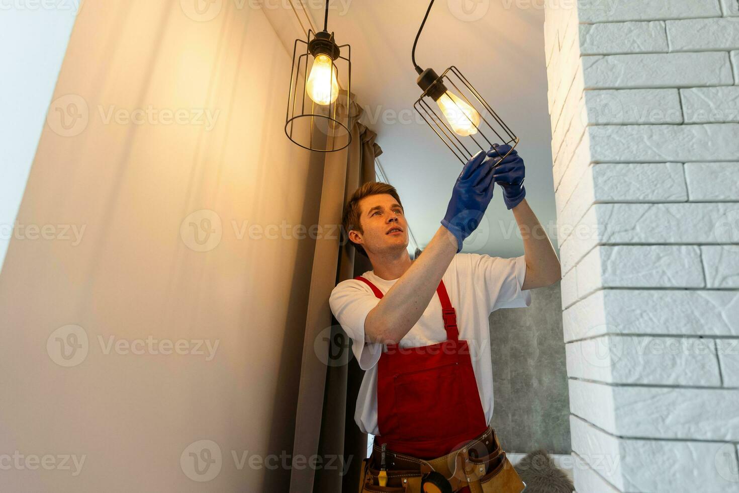 Worker installing lamp on stretch ceiling indoors. photo