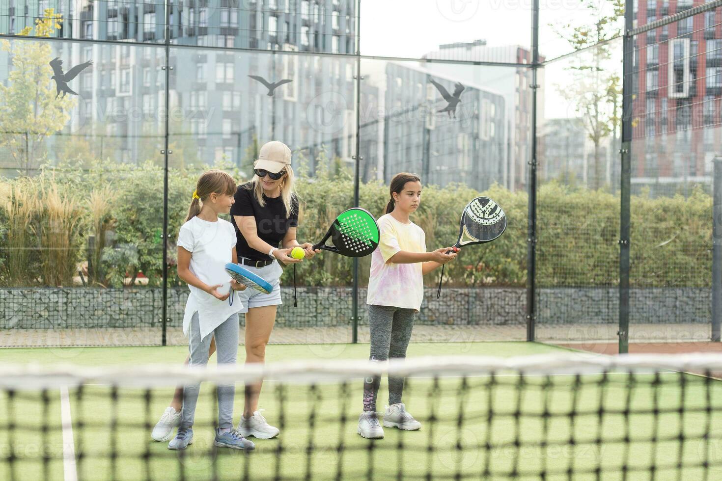 Cheerful coach teaching child to play tennis while both standing on tennis court photo