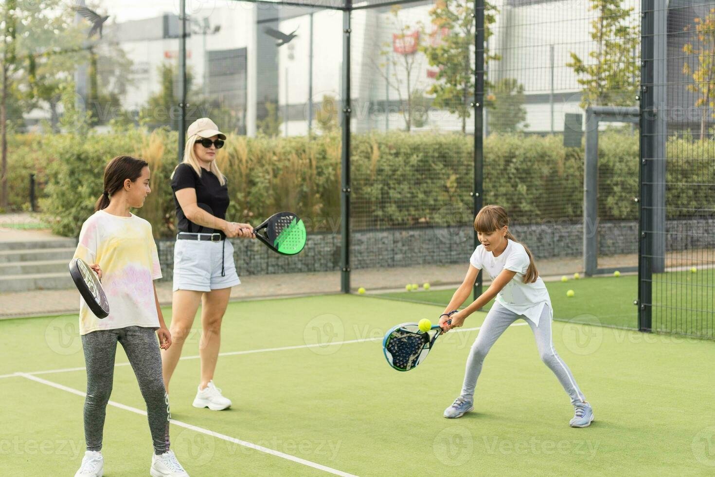 Cheerful coach teaching child to play tennis while both standing on tennis court photo