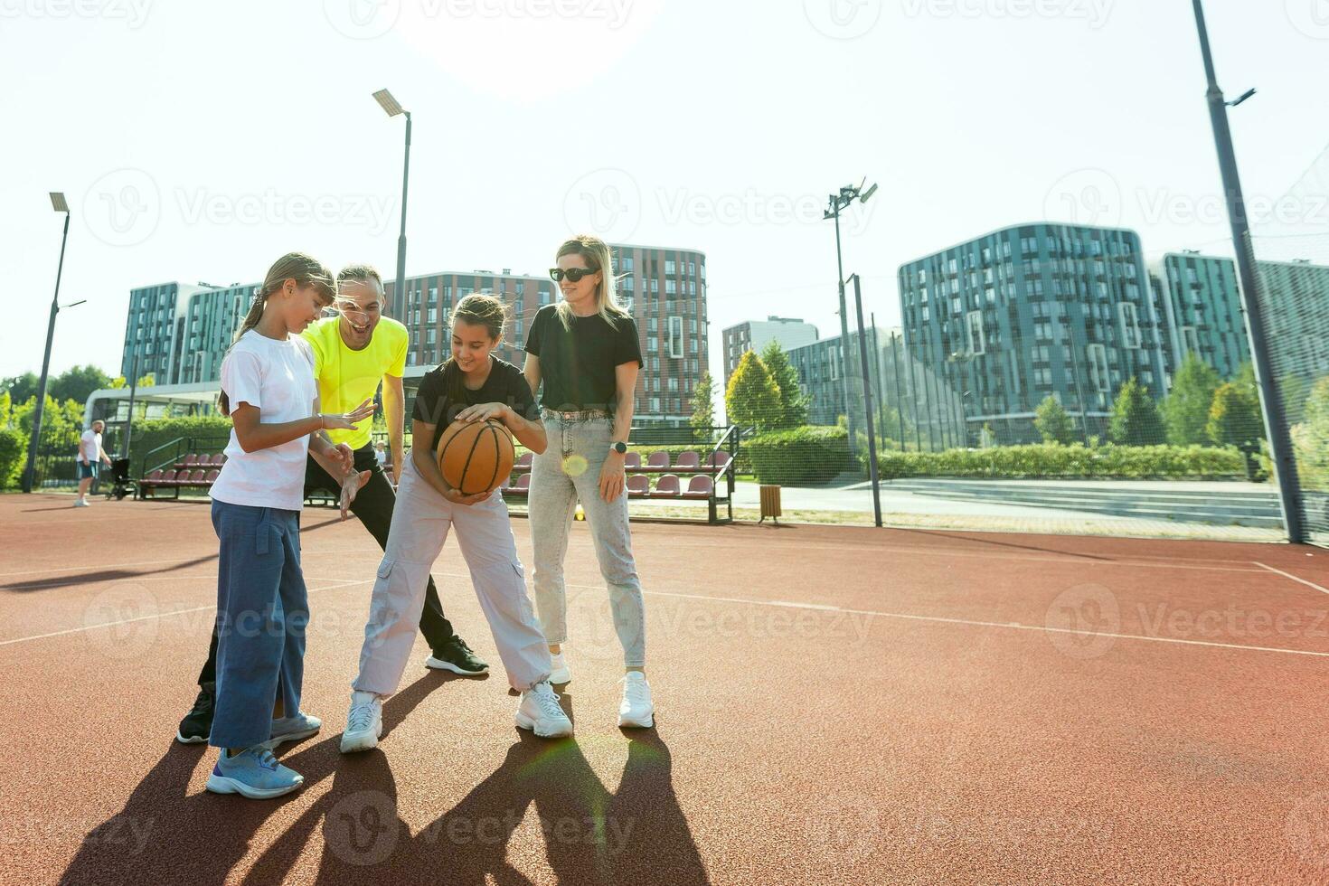 summer holidays, sport and people concept happy family with ball playing on basketball playground photo