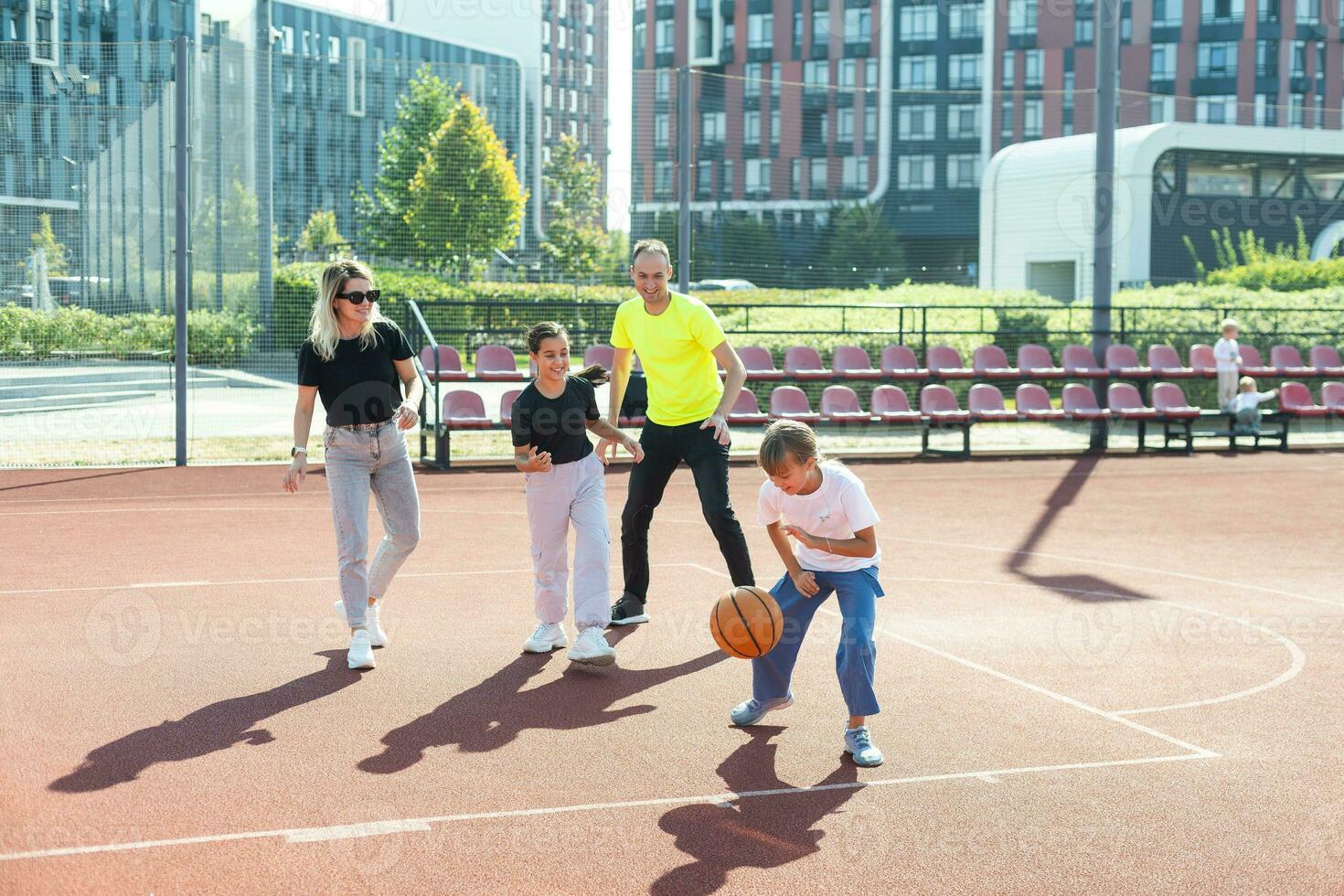 summer holidays, sport and people concept happy family with ball playing on basketball playground photo