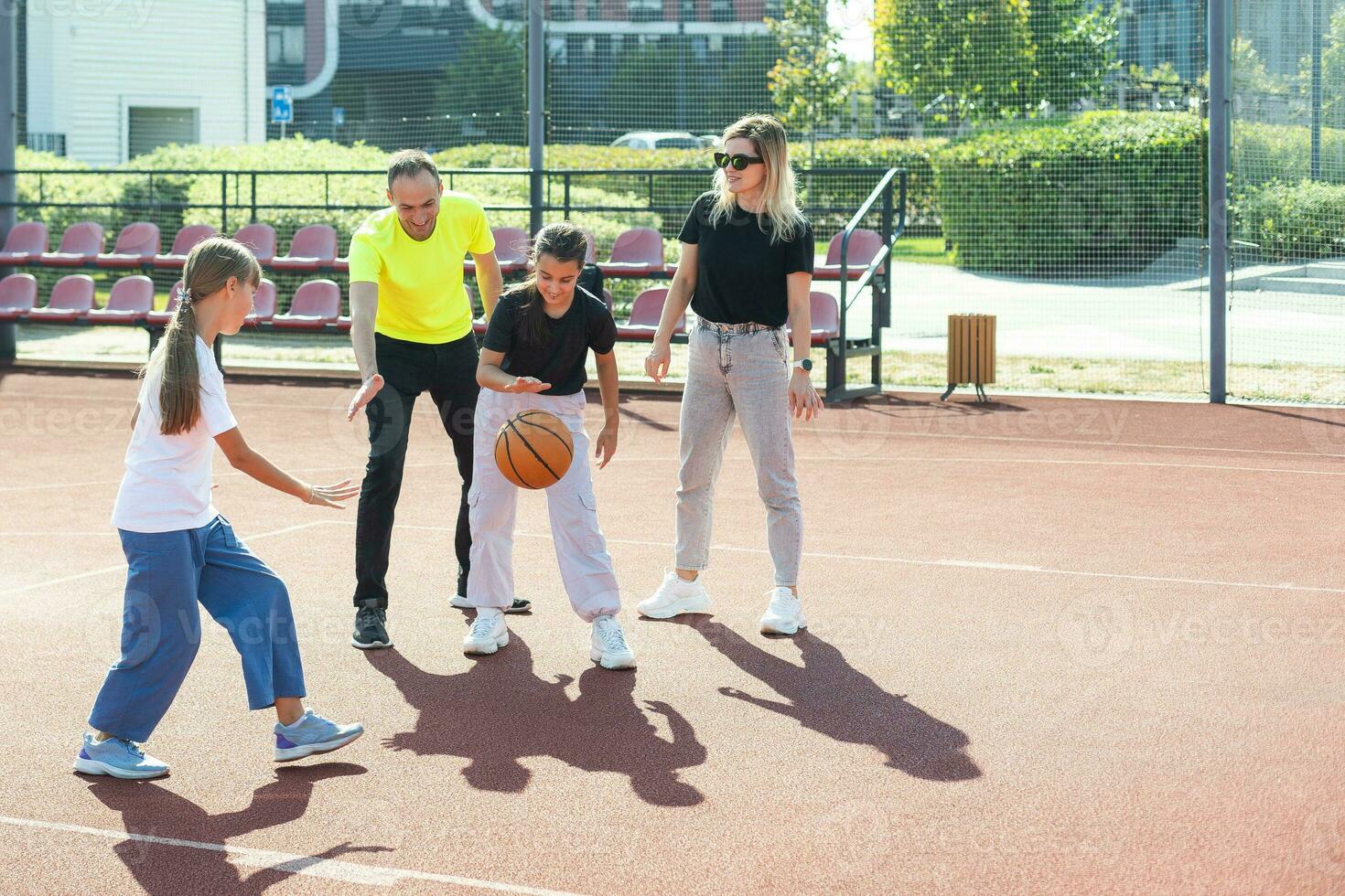 summer holidays, sport and people concept happy family with ball playing on basketball playground photo