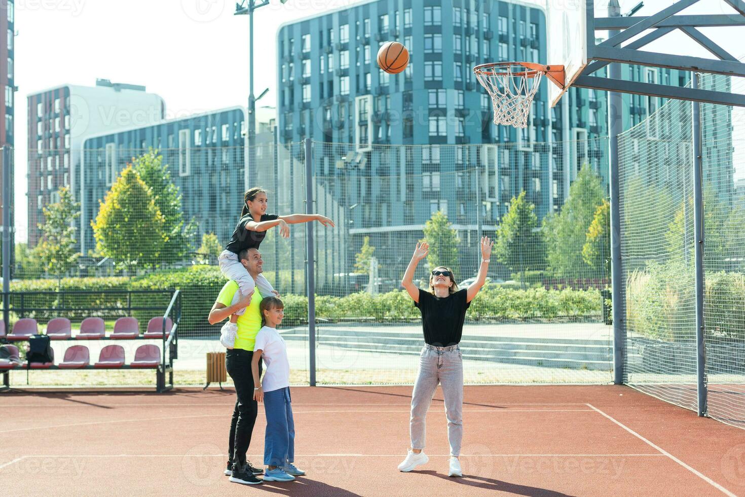 summer holidays, sport and people concept happy family with ball playing on basketball playground photo