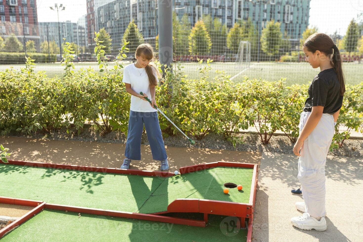 linda colegio niña jugando mini golf con familia. contento niñito niño teniendo divertido con al aire libre actividad. verano deporte para niños y adultos, al aire libre. familia vacaciones o complejo. foto