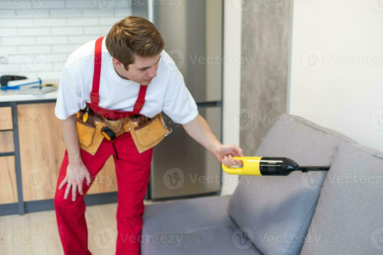 Handsome young man cleaning furniture. Process of deep furniture cleaning, removing dirt from sofa. Washing concept photo