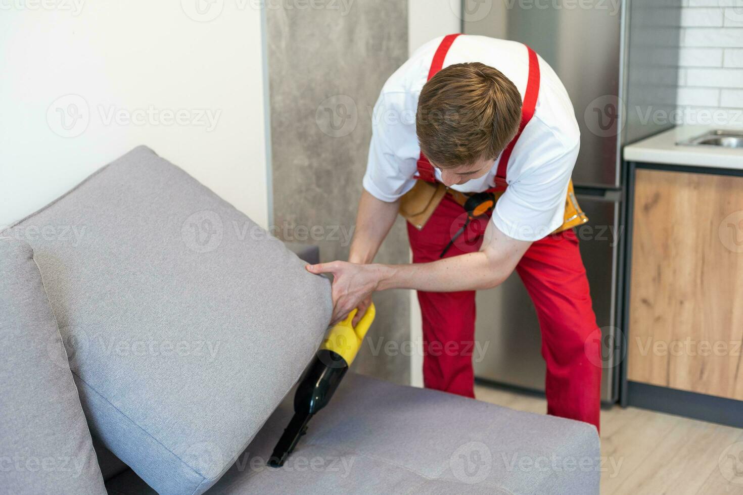 Handsome young man cleaning furniture. Process of deep furniture cleaning, removing dirt from sofa. Washing concept photo