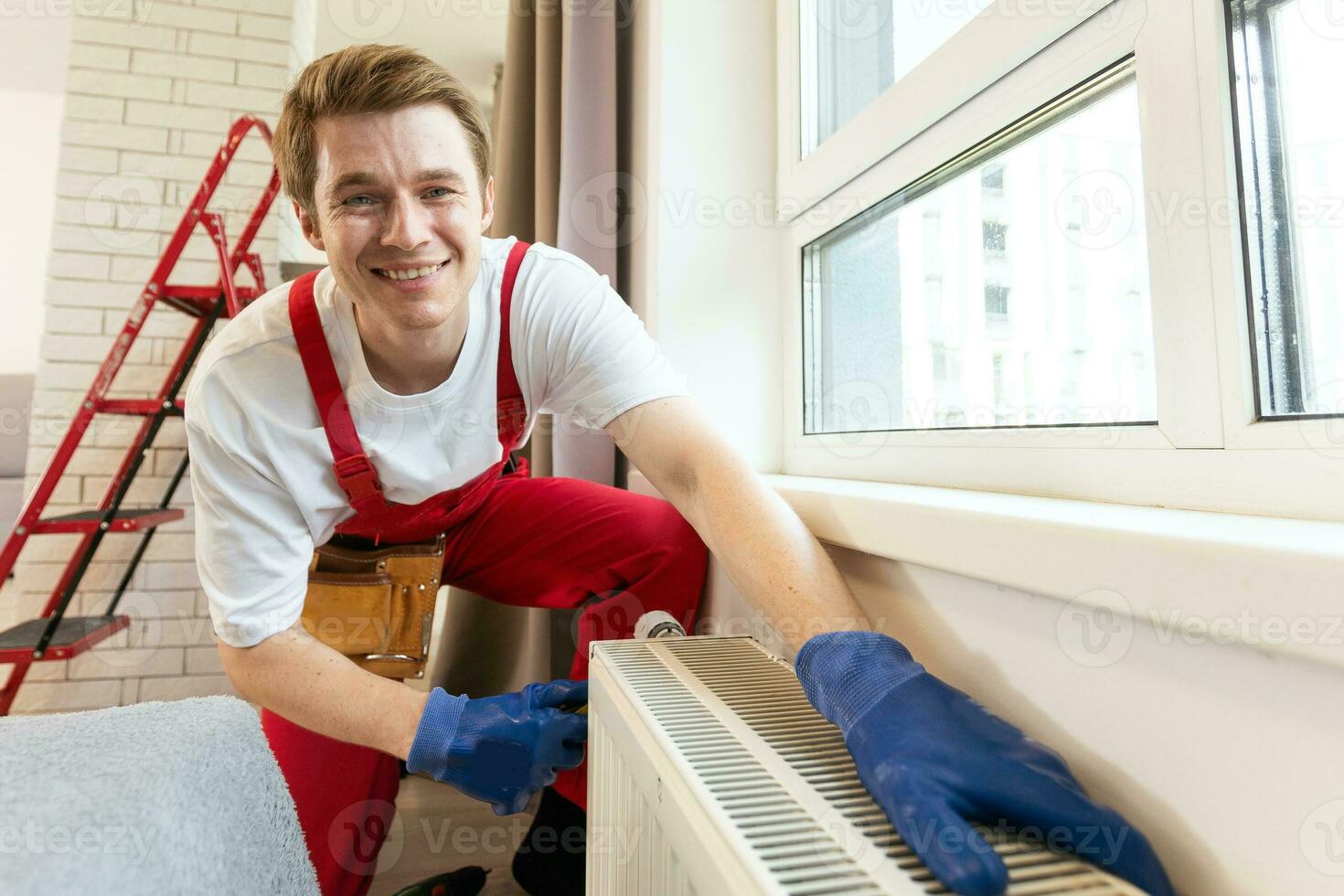 A plumber is fixing a radiator. With an adjustable wrench, he tightens the tap. A briefcase with a tool at hand photo