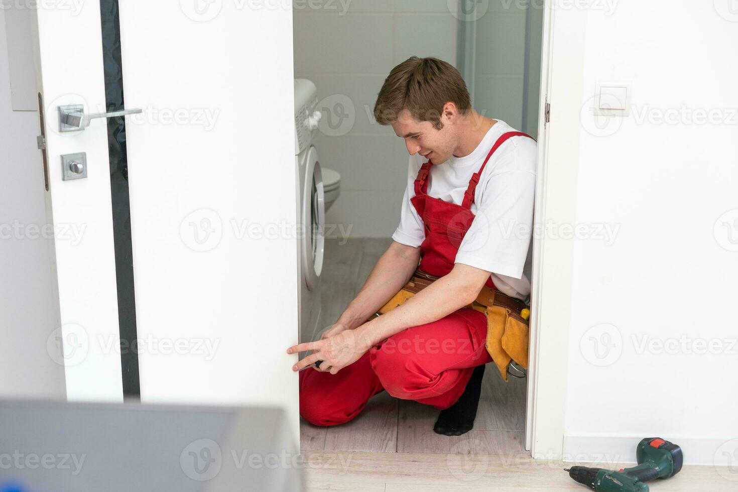 Repair Service Concept. Portrait of smiling handsome young locksmith in blue uniform installing door knob on front wooden entrance door at home or office workplace. photo