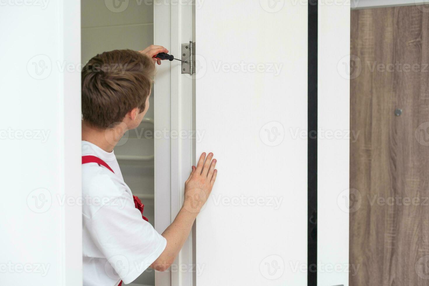 joven manitas instalando una puerta blanca con un taladro eléctrico en una habitación foto