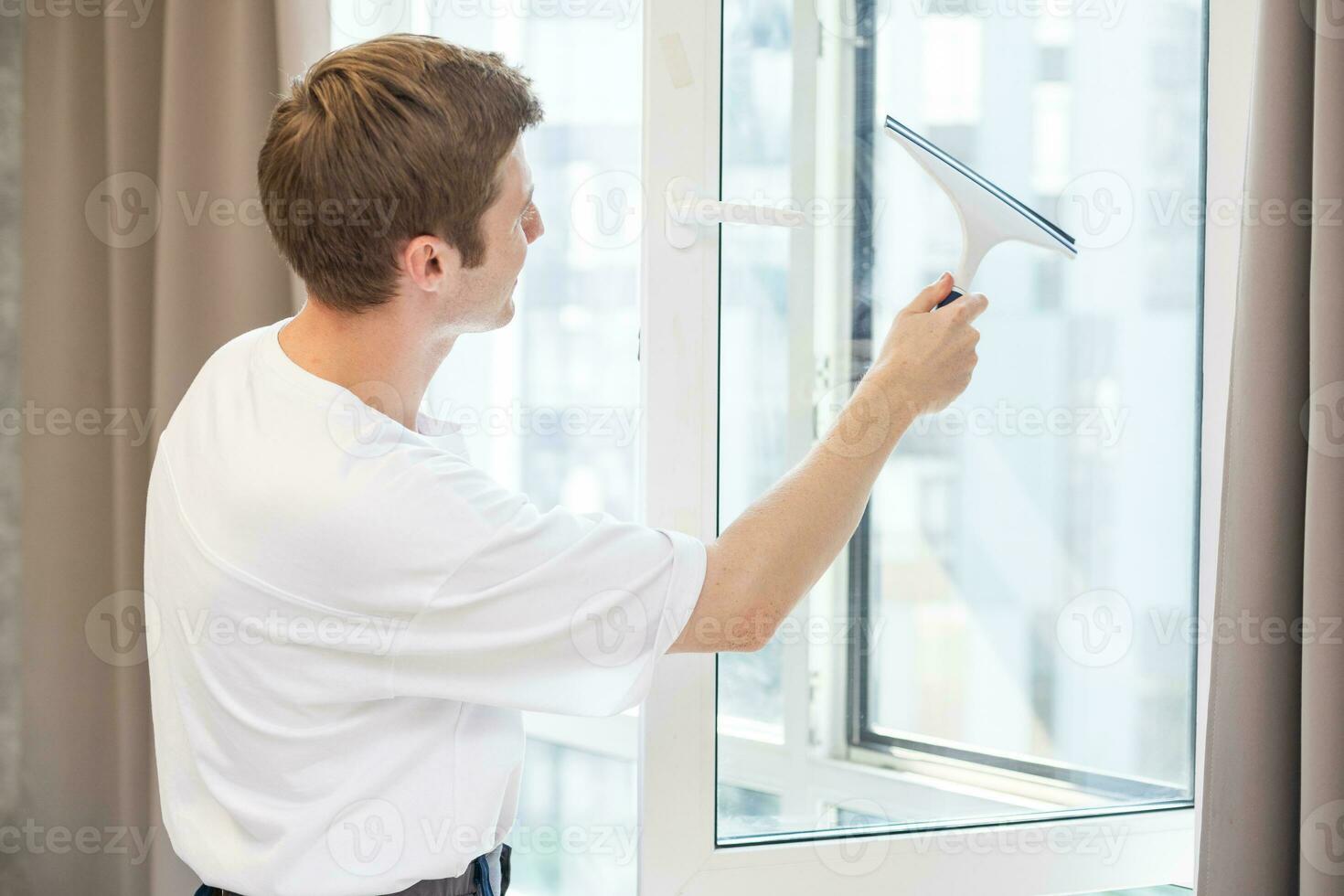 joven hombre limpieza ventanas en el casa foto