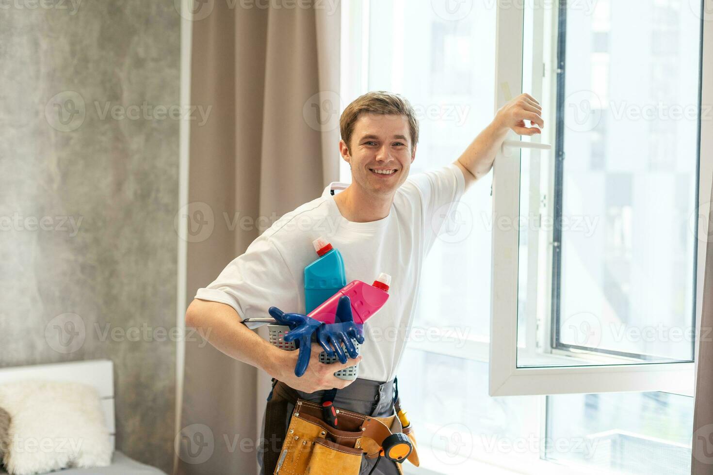 Side view of smiling man with bottle of detergent and rag cleaning window at home photo