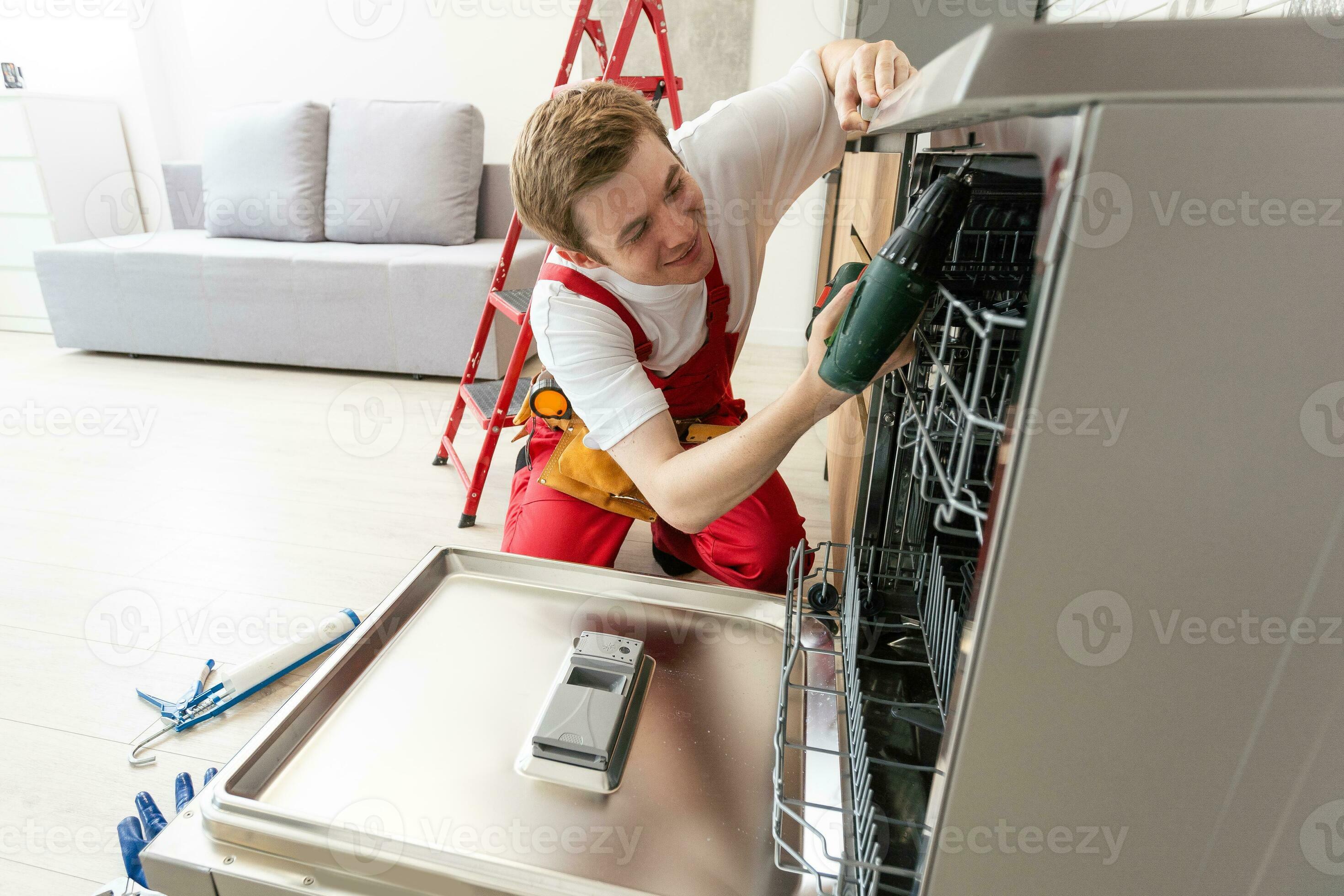 Technician or worker in uniform installs dishwasher into the kitchen