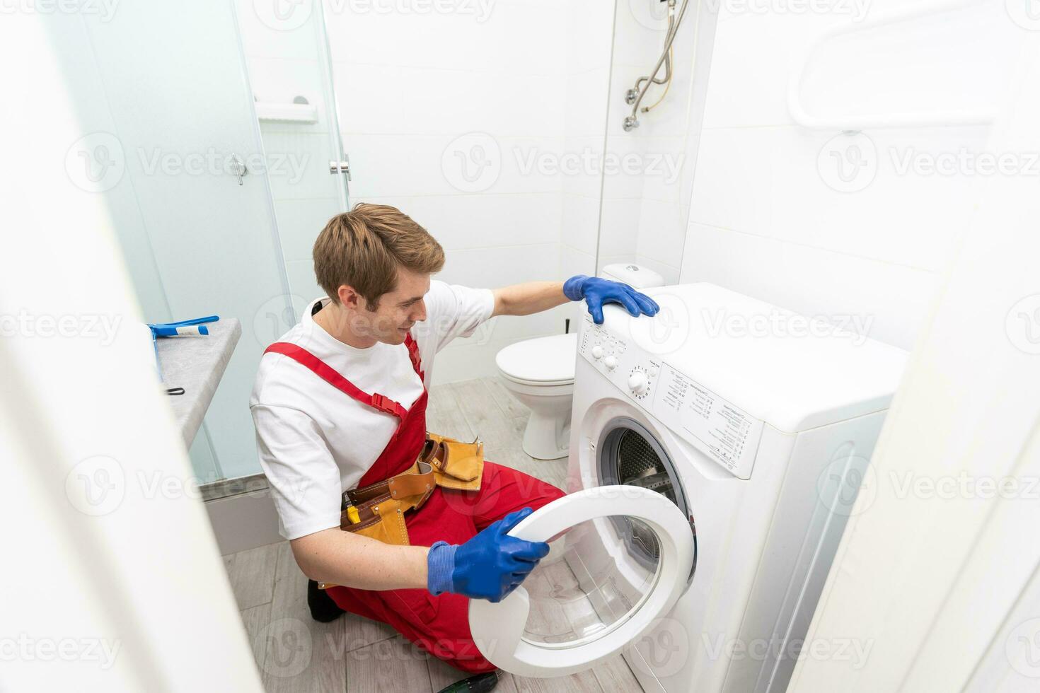 The young handsome repairman in worker suit with the professional tools box is fixing the washing machine in the bathroom. photo