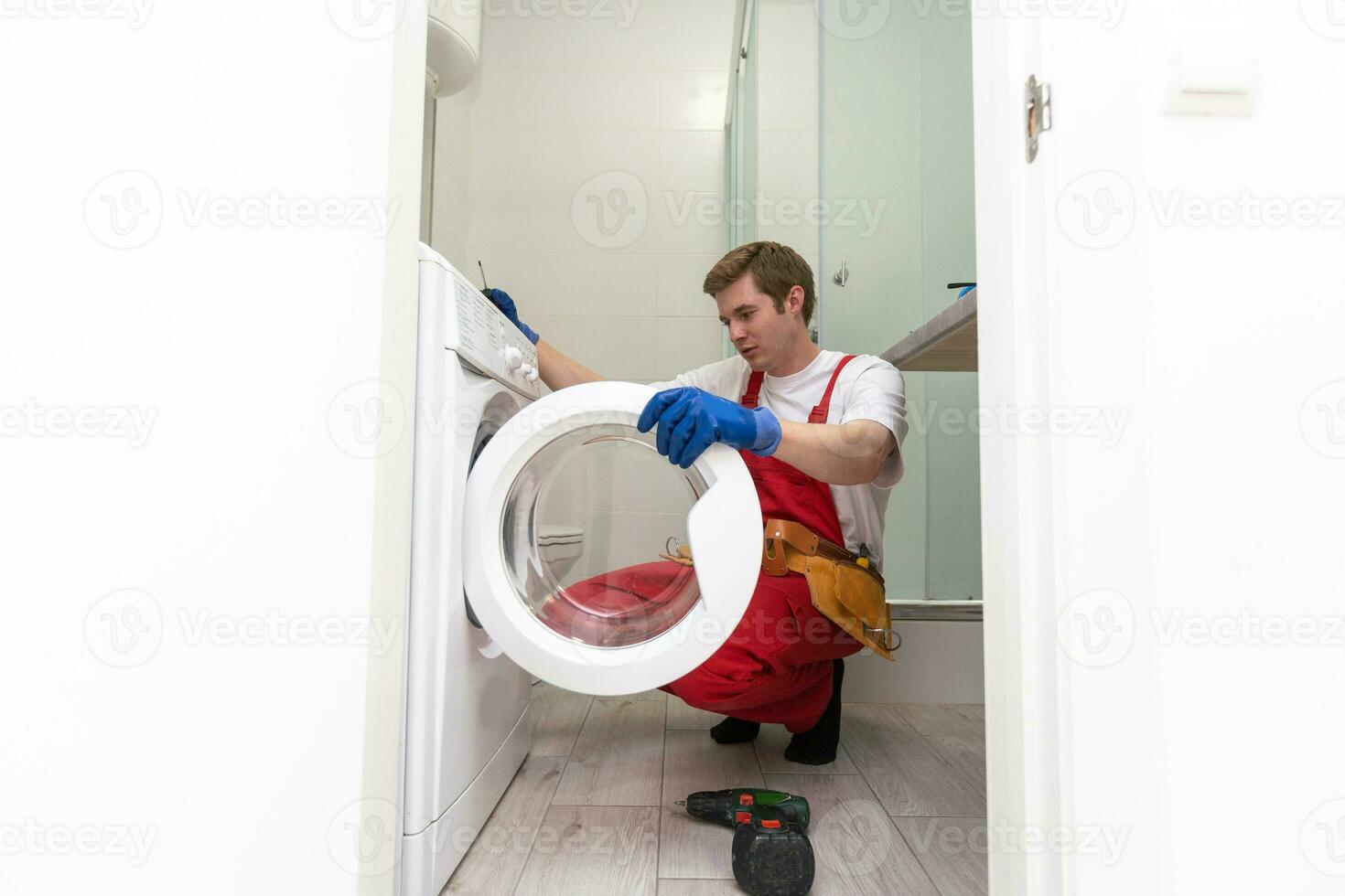 The young handsome repairman in worker suit with the professional tools box is fixing the washing machine in the bathroom. photo