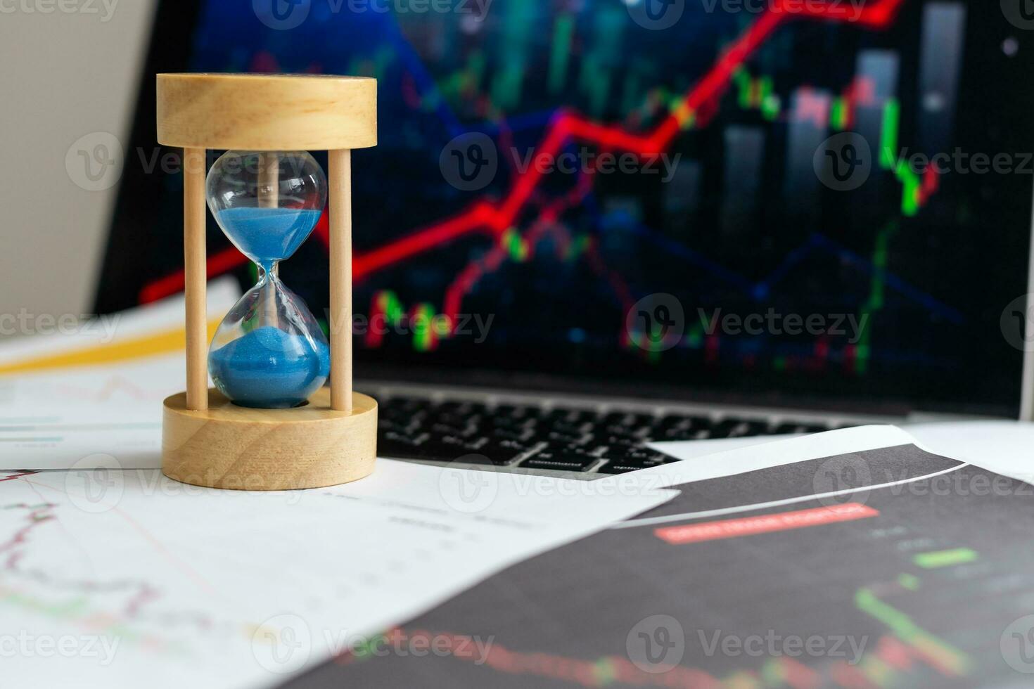 Hourglass and stacks of gold coins on the background of financial charts and graphs. photo