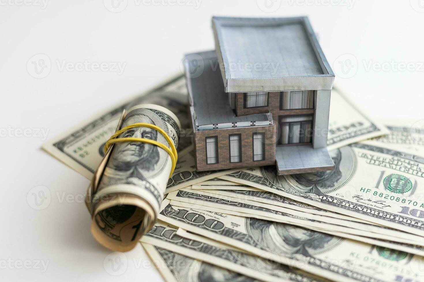 A small house lies on a fan of hundred dollar bills. The keys to the purchased house. Reduced copy of the house on a white background photo