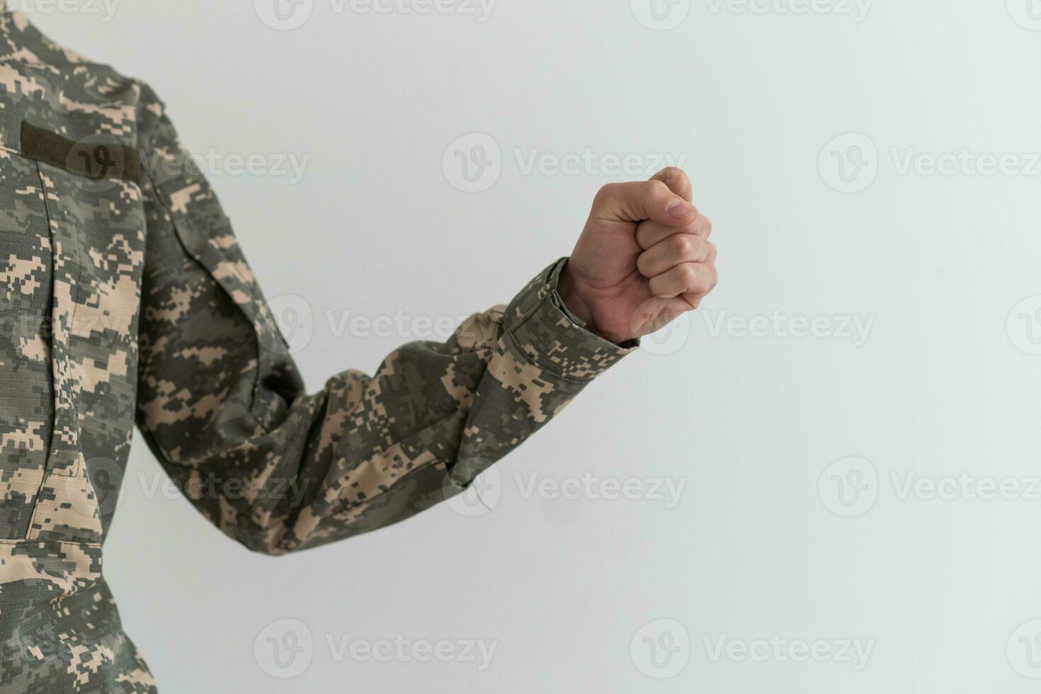 Hand in camouflage shows gesture on gray background. Fingers clenched into a fist. Freeze gesture in the military. Army gesture language. photo