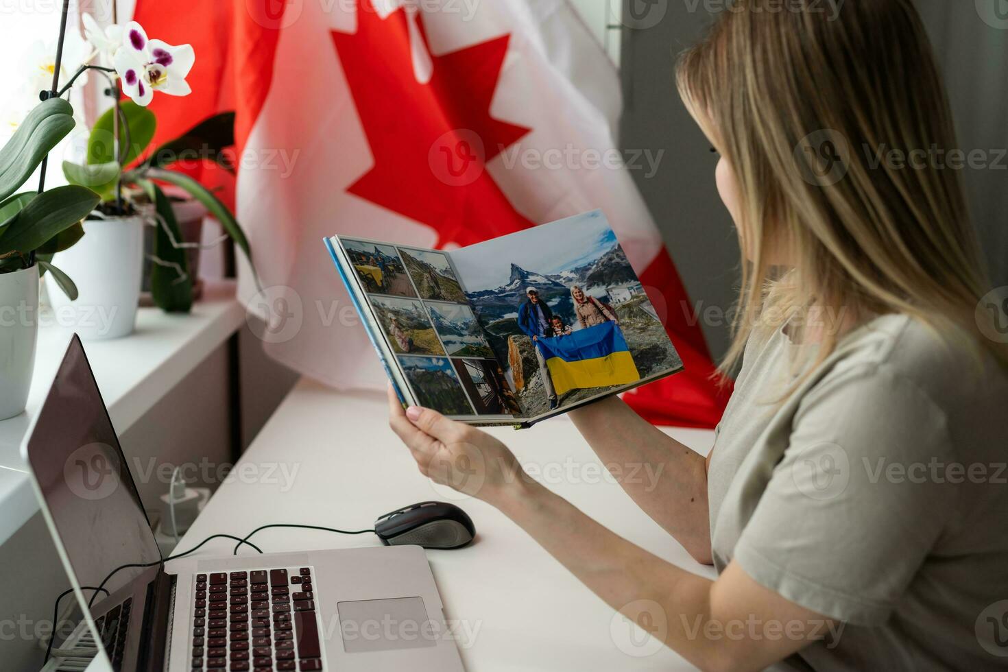 A female hand holds a small canada flag and a laptop on the background of the university. Close up photo