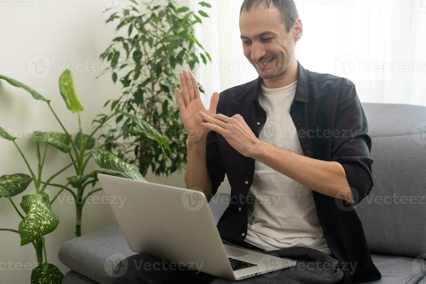 Happy smiling deaf young caucasian man uses sign language while video call using laptop while sitting at home, virtual communication concept. photo