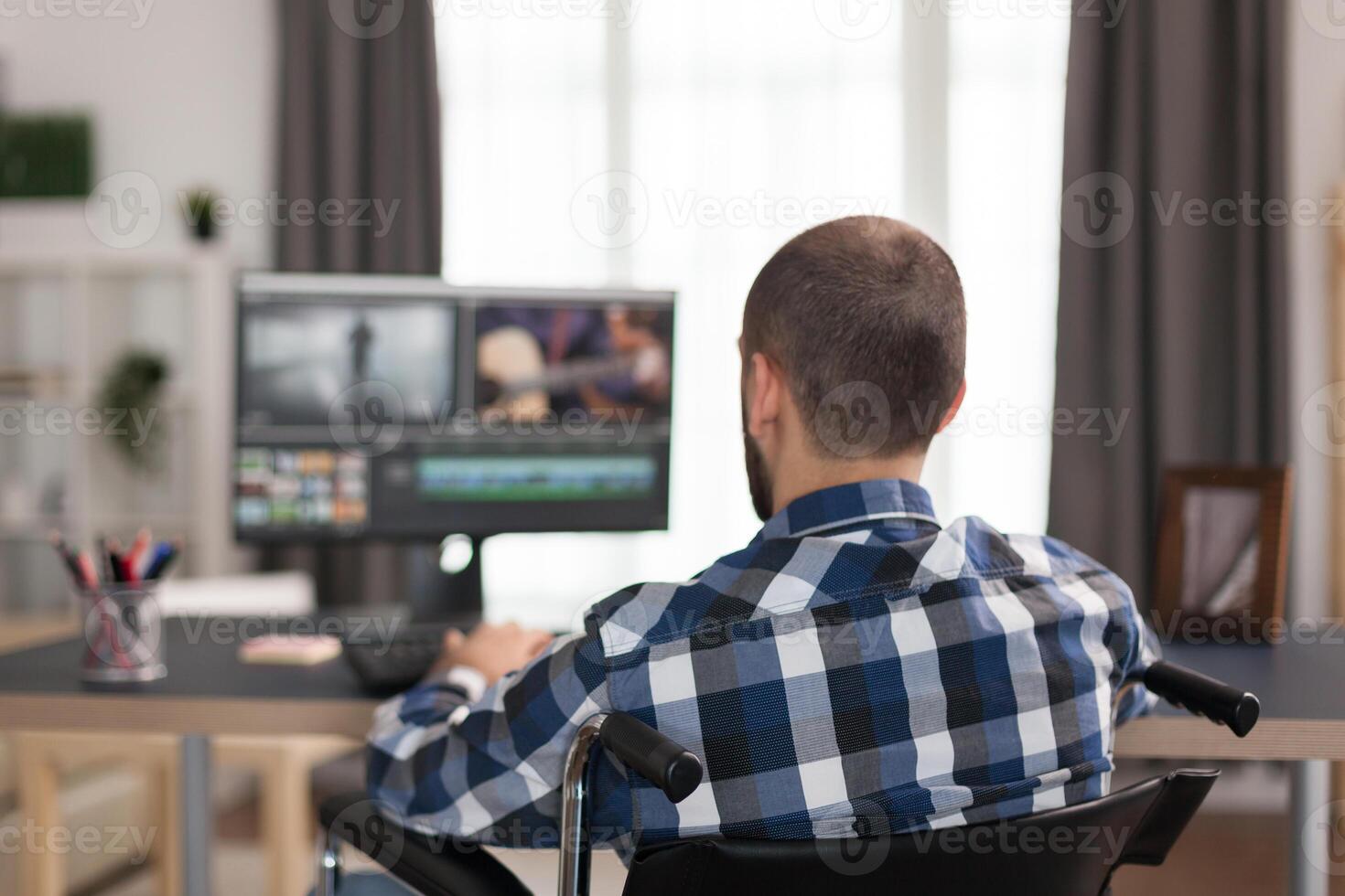 Handicapped film maker in wheelchair working film post production. Invalid videographer doing his business online, using high technology, sitting in his apartment, working remotely in special conditions. photo