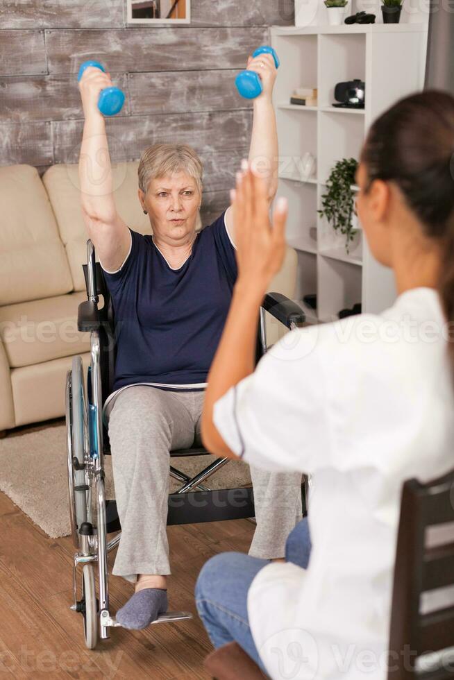 Nurse explaining dumbbell exercises for disabled elderly woman. Handicapped old person recovering professional help nurse, nursing retirement home treatment and rehabilitation photo