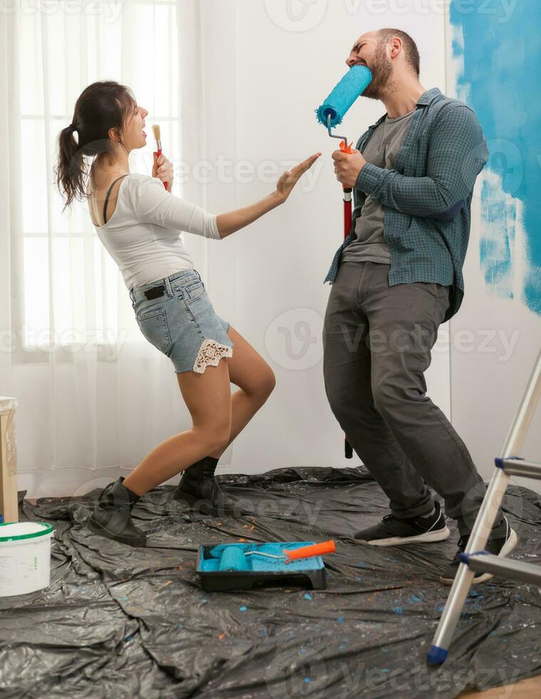 Funny couple decorating living room and sing on renovation tools. Apartment redecoration and home construction while renovating and improving. Repair and decorating photo